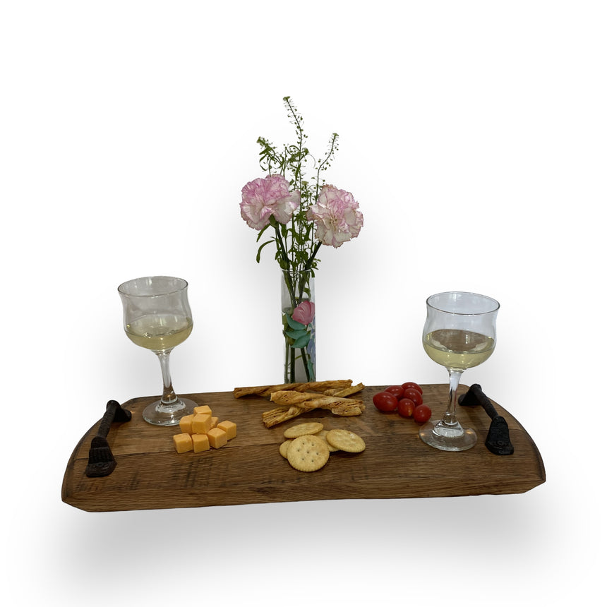 Two glasses of white wine, cheese, crackers, and tomatoes sit on the Charcuterie and Cheese Rectangle Wooden Serving Board (Full Size, Hand Made Solid Wood), with flowers in a vase behind.