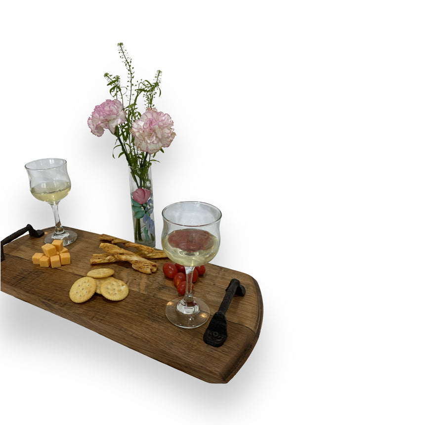 The Charcuterie and Cheese Rectangle Wooden Serving Board, hand made from solid wood, beautifully displays wine, cheese, crackers, tomatoes, and pink flowers on a white background—perfect for adding rustic charm to any gathering.