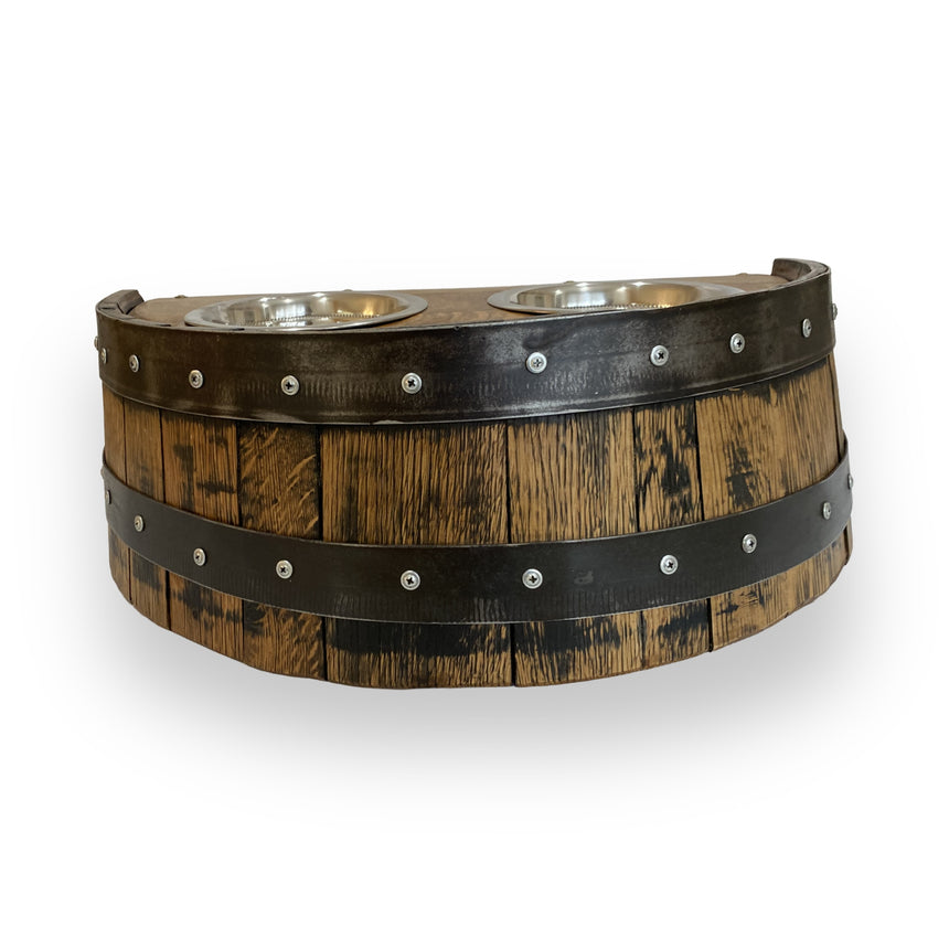 The Whiskey Barrel Pet Feeder features two metal bowls and dark metal bands for rustic style while keeping mealtime tidy. Its half-barrel design adds charm, shown here on a white background.