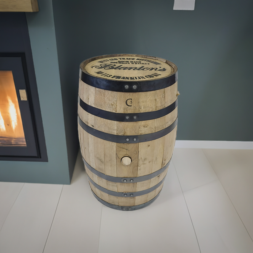 A Clean Full Barrel With Logo Head featuring metal bands is displayed on a light floor beside a fireplace in a modern room.