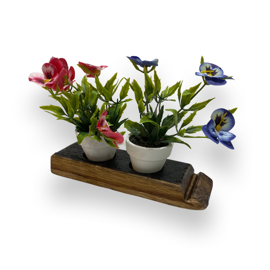 Two small potted plants with pink and blue flowers rest in Double Bud Vase Whiskey Staves, creating a charming display on a rustic stand against a white background.
