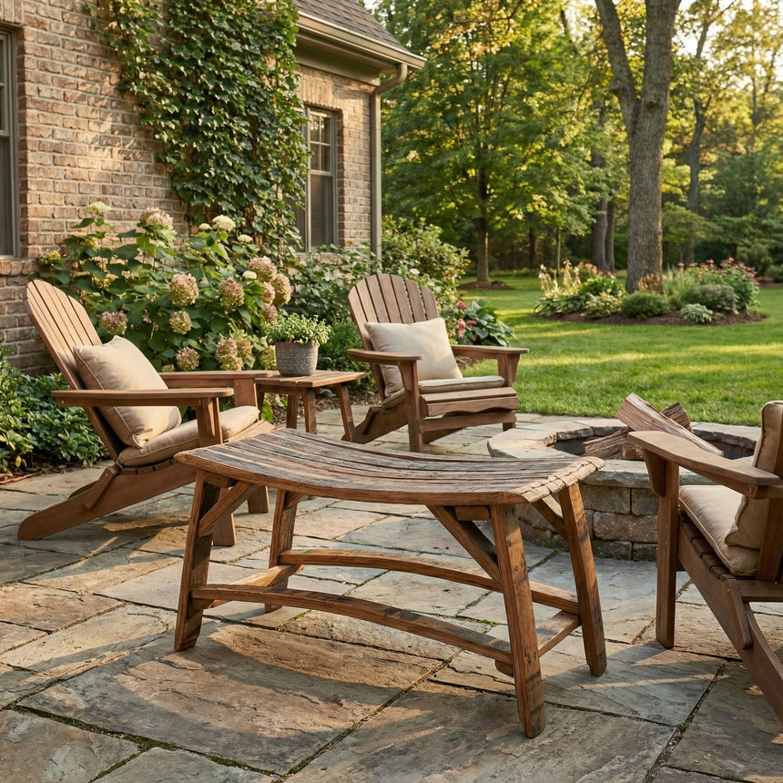 Wooden Adirondack chairs and a Barrel Stave Bench surround a fire pit on a stone patio in a lush, green backyard.