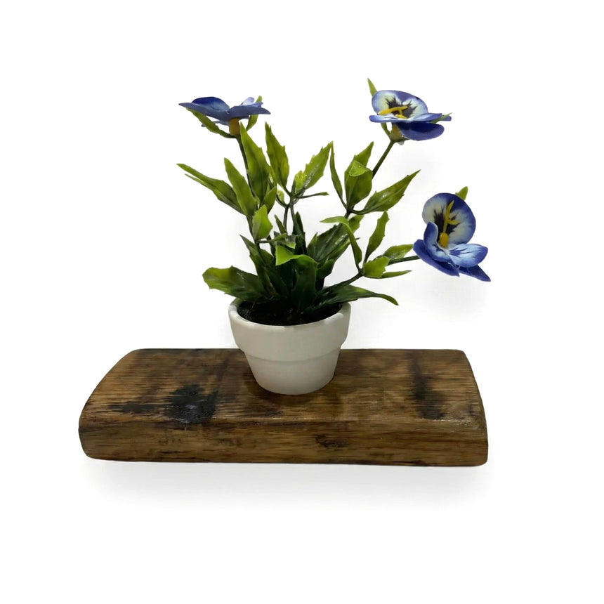 Single Bud Vase Whiskey Barrel Stave featuring a small white pot with blue artificial flowers and green leaves, set on a rustic reclaimed barrel stave shelf against a white background.