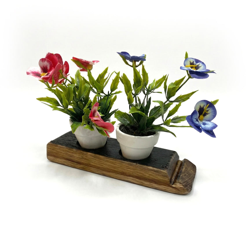Two small potted plants with pink and blue flowers sit on a Double Bud Vase Whiskey Staves stand, adding a rustic touch to your home decor against a white background.
