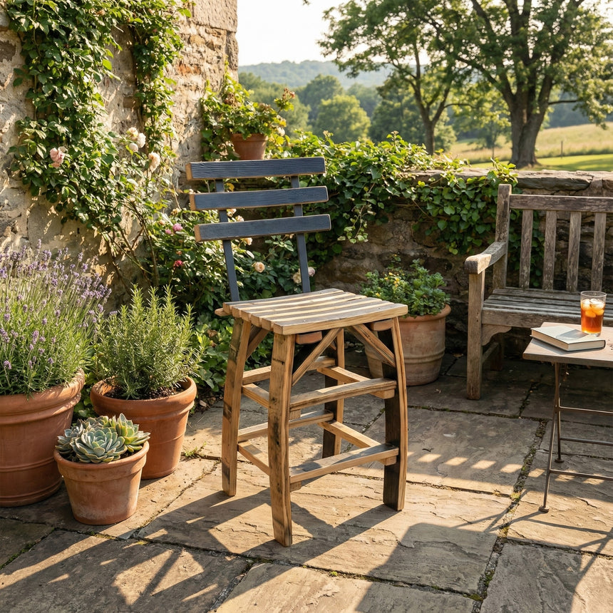 A hand made solid wood Barstool Chair with backrest, crafted from barrel staves, sits on a sunny stone patio amid potted plants and lush greenery.