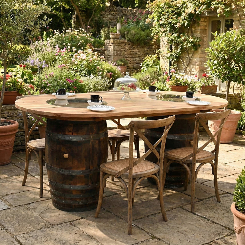 The Double Barrel Table set with four chairs is arranged in a lush garden patio, surrounded by blooming flowers.
