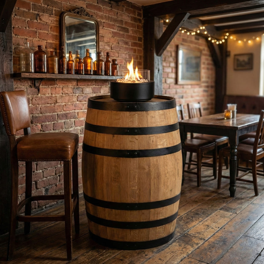 The Pub Table Glass Fire Top, crafted from a whiskey barrel with a built-in tabletop fire, adds charm to a rustic pub setting featuring brick walls and vintage decor.