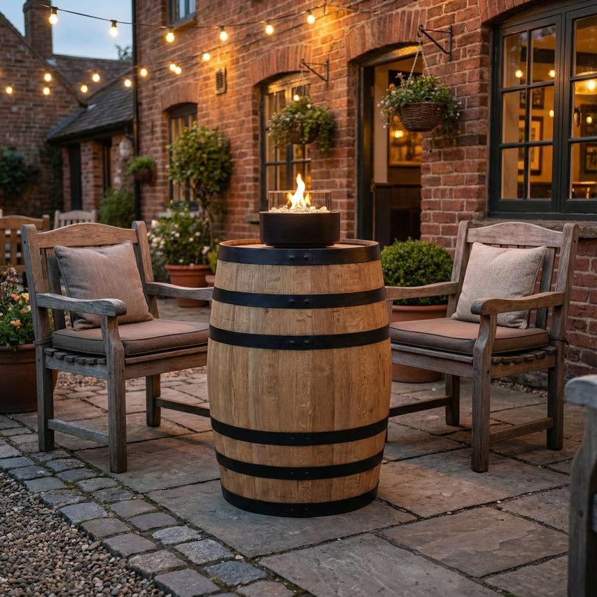 Two wooden chairs sit beside a Pub Table Glass Fire Top, creating a cozy outdoor patio scene under string lights.