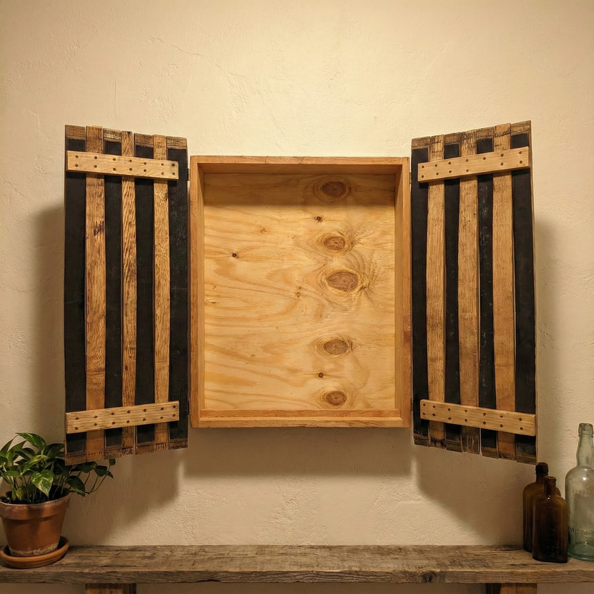 The handcrafted Dart Board Cabinet, made from solid wood barrel staves and fitting a standard tournament spec dart board, sits above a shelf with decor—an ideal game room accent.