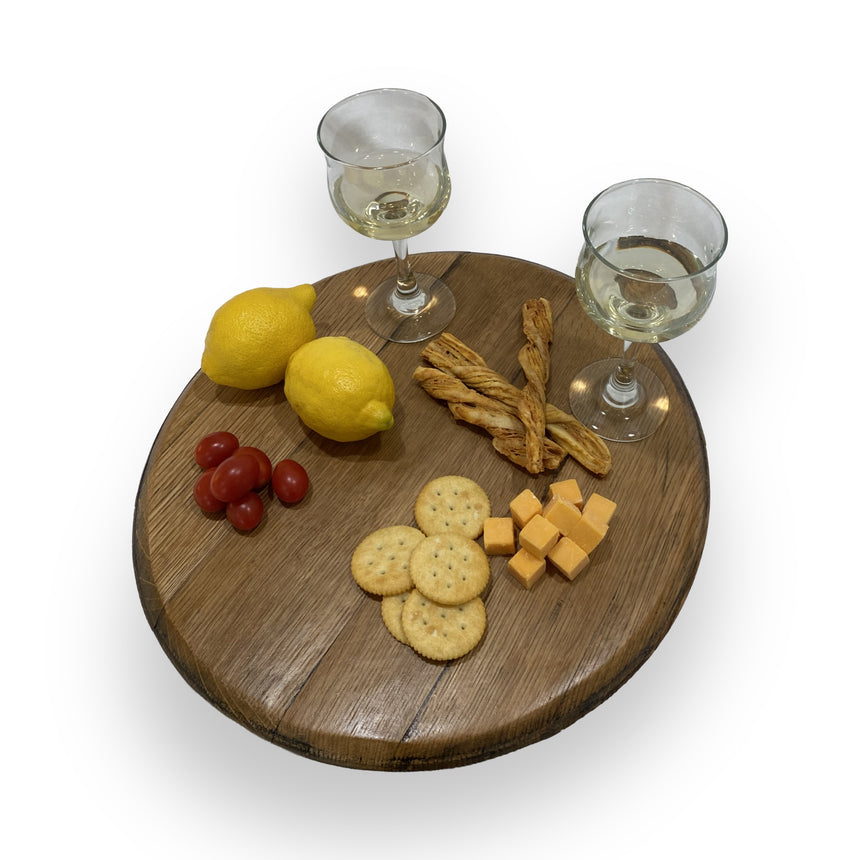 Two glasses of white wine, lemons, breadsticks, tomatoes, crackers, and cheese are arranged on the Lazy Susan Round Swivel Wooden Tray, hand made from solid wood with a barrel head construction.