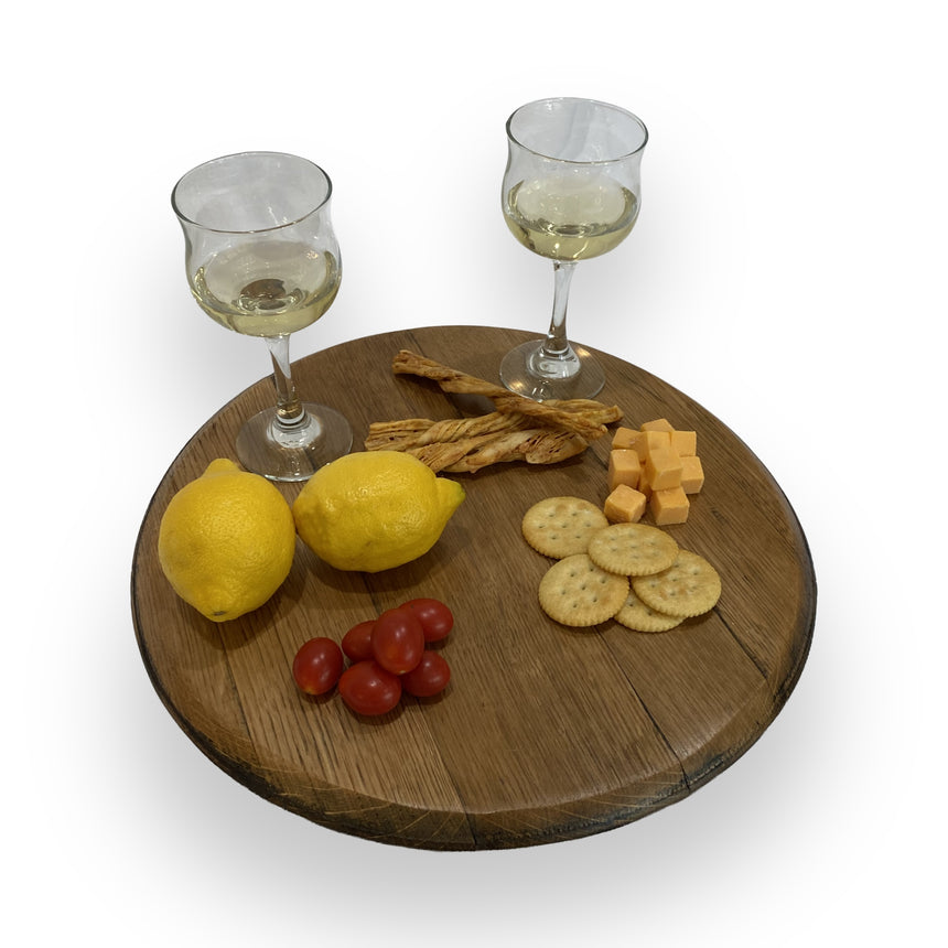 Two glasses of white wine with cheese, crackers, breadsticks, lemons, and tomatoes are beautifully arranged on the Lazy Susan Round Swivel Wooden Tray, Hand Made Solid Wood Barrel Head Construction.