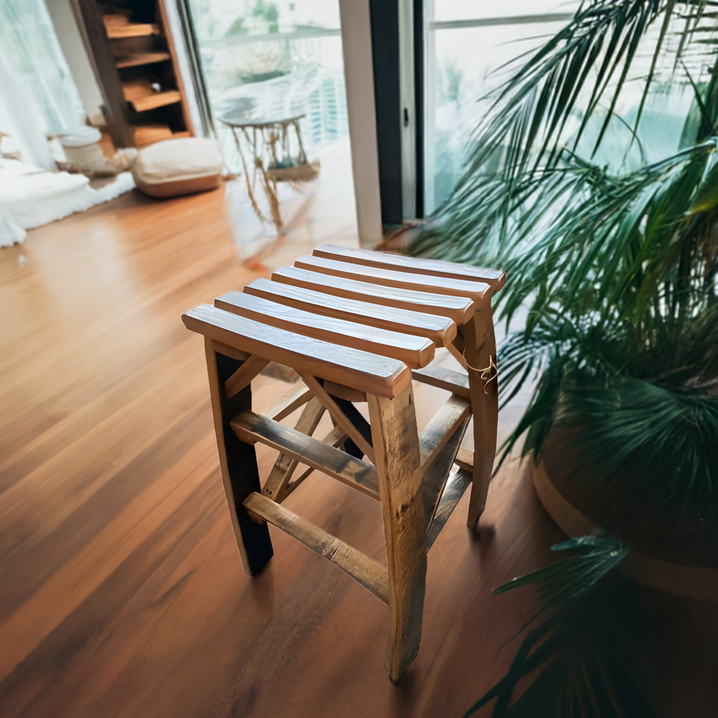 The Whiskey Barrel Stave Bar Stool, crafted with sturdy construction, sits on a wooden floor by a large window and indoor plants, adding rustic elegance to the room.