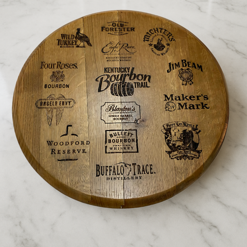 The Whiskey Barrel Head Etch Bourbon Trail is a round wooden board made from authentic whiskey barrel heads, engraved with Kentucky bourbon logos—a perfect keepsake from the Bourbon Trail, shown on a white marble surface.