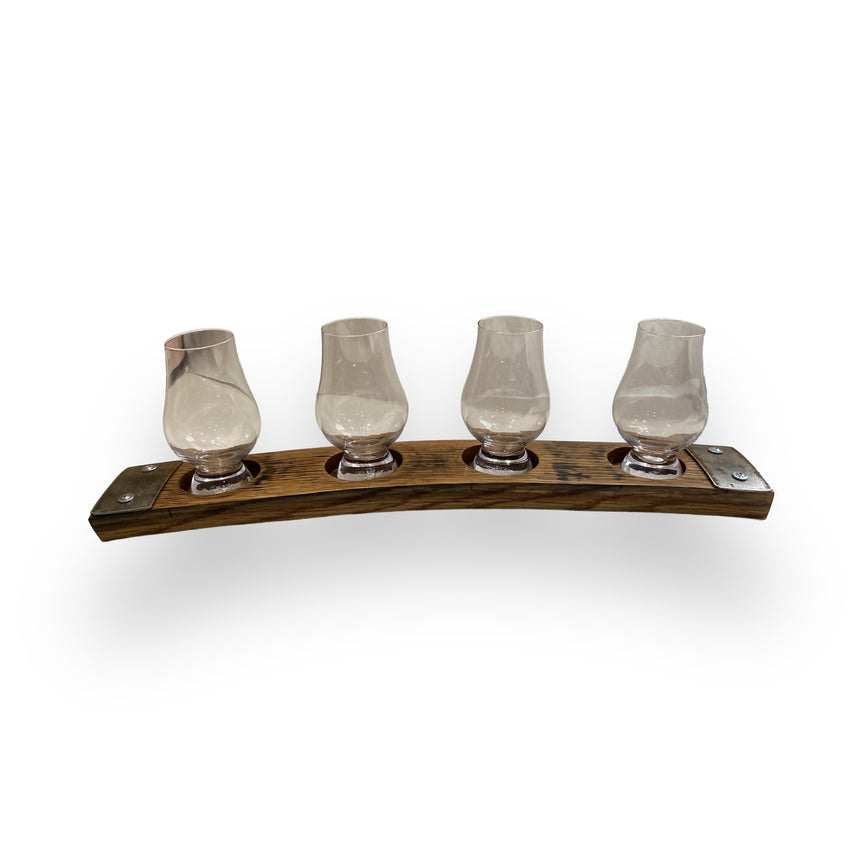 The Whiskey Tasting Flight Board for 4 Glasses features hand made solid wood construction and metal accents, crafted from authentic whiskey barrels. Four empty glasses sit on the curved board, displayed on a white background for rustic charm.