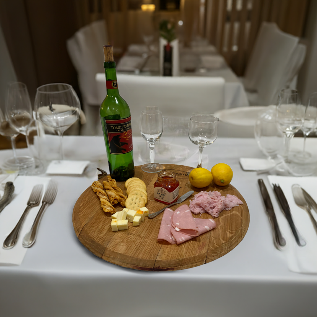 An elegant display of wine, cheeses, ham, bread, and lemons is arranged on a formal table using the Wine Barrel Head Charcuterie board, highlighting artisan craftsmanship.