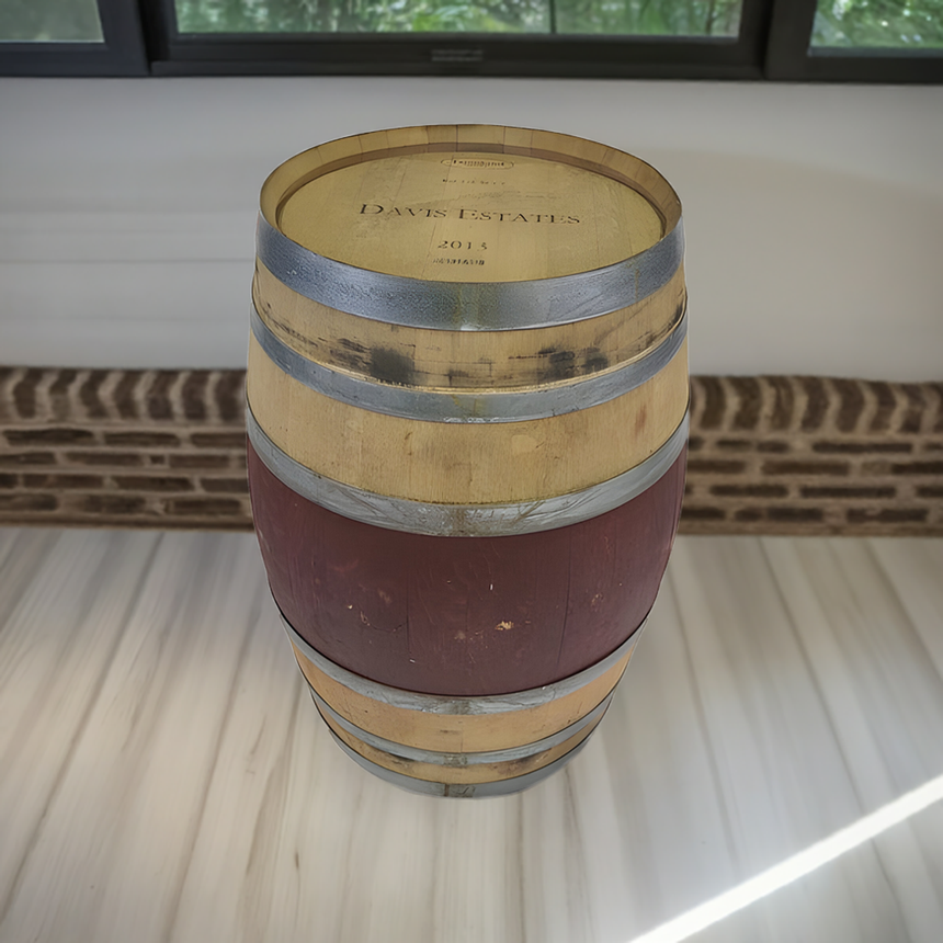 A Wine Barrel labeled "Davis Estates 2015" stands on a light floor near a brick wall and windows, showcasing rustic appeal with classic American Oak Barrels craftsmanship.