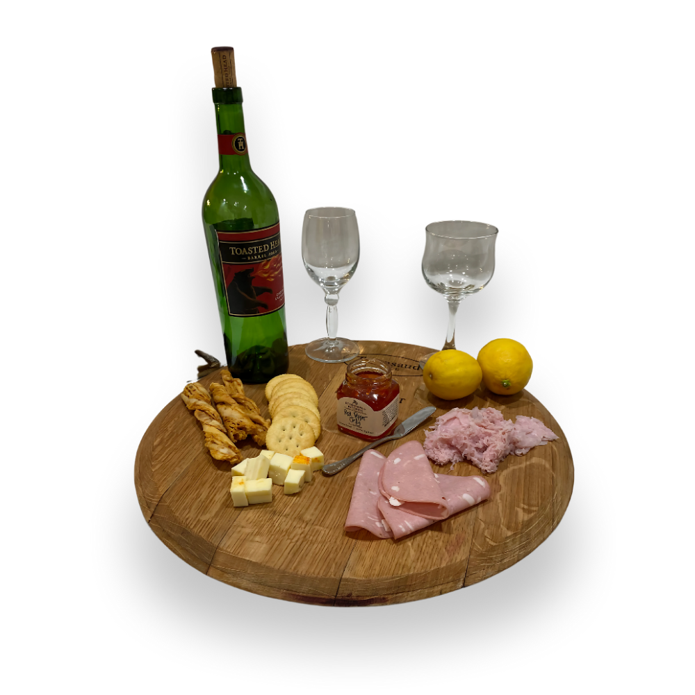 A wine and charcuterie spread with wine, glasses, crackers, meats, cheese, breadsticks, lemons, and jam—elegantly arranged on the artisan-crafted Wine Barrel Head Charcuterie board.