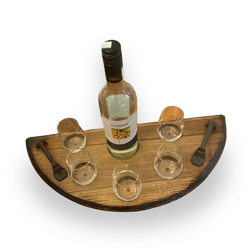 The Wine Tasting Tray is a rustic wooden piece made from handcrafted barrel heads, designed to hold one liquor bottle, six glasses, and two metal keys on top.