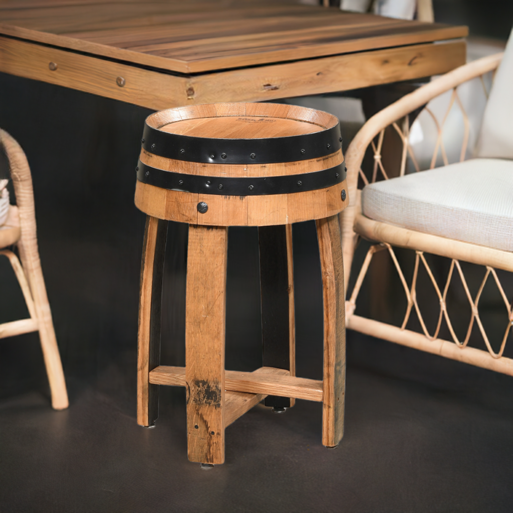 The Wooden End Table, crafted from reclaimed wood with a barrel-shaped top and black metal bands, sits beside wicker chairs and a wooden table, enhancing the rustic charm of the space.