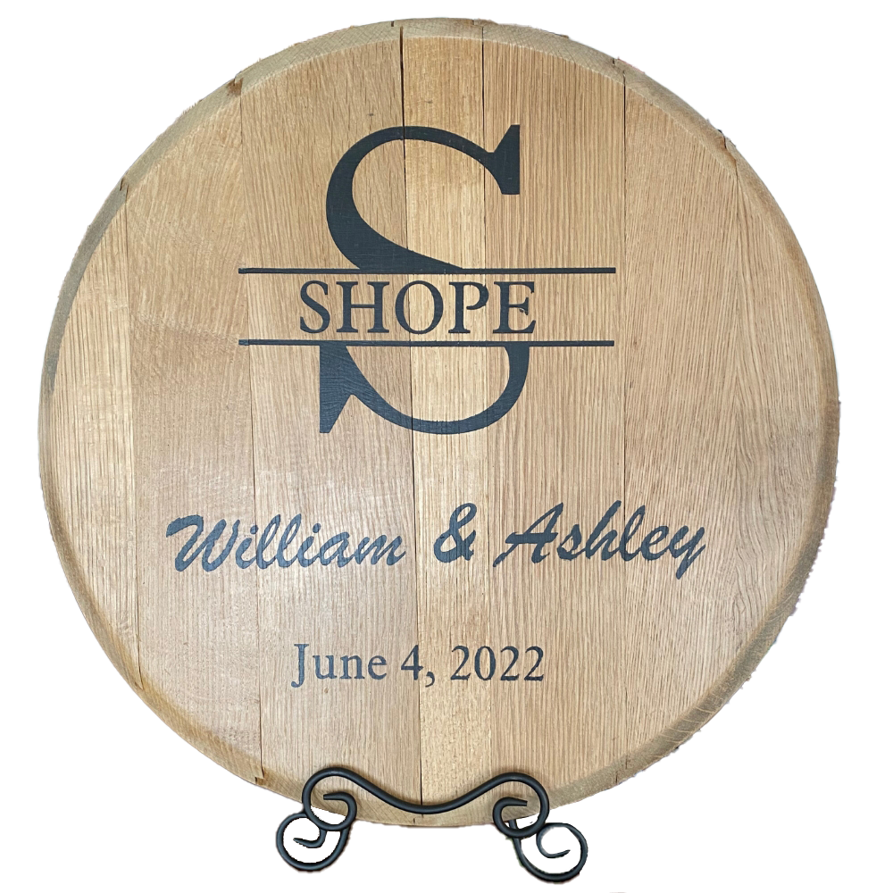 The Whiskey Barrel Head Wedding Special is a round wooden sign made from authentic whiskey barrel heads, personalized with names "William & Ashley," the surname "Shope," and engraved wedding date "June 4, 2022" in black text.