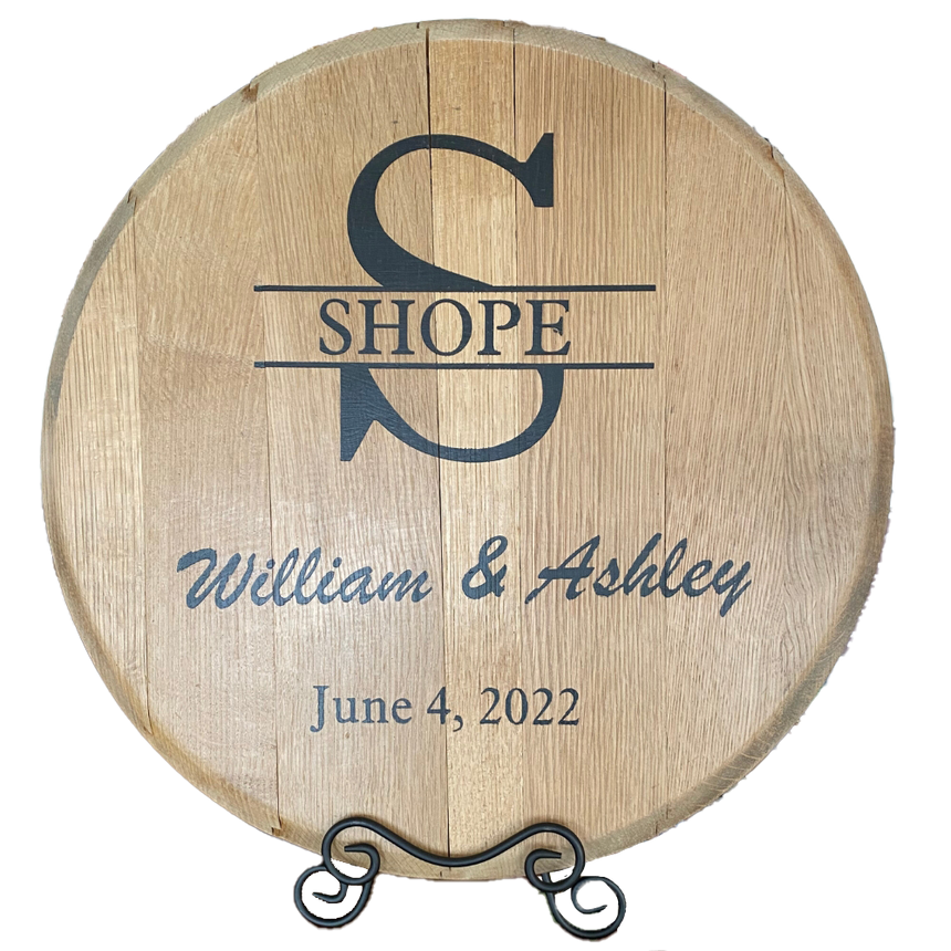 The Whiskey Barrel Head Wedding Special is a round wooden sign made from authentic whiskey barrel heads, personalized with names "William & Ashley," the surname "Shope," and engraved wedding date "June 4, 2022" in black text.