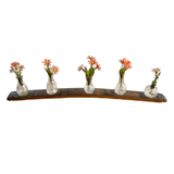 Five glass vases with orange flowers are arranged on a Bud Vase Stand, bringing rustic charm to the curved wooden shelf.