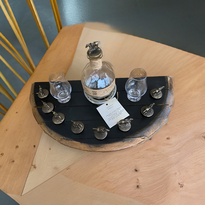 A Bar Tray, hand made from solid wood barrel and designed to fit a Blanton's bottle and horse cork stoppers (corks not included), sits on a geometric wooden table with two glasses.