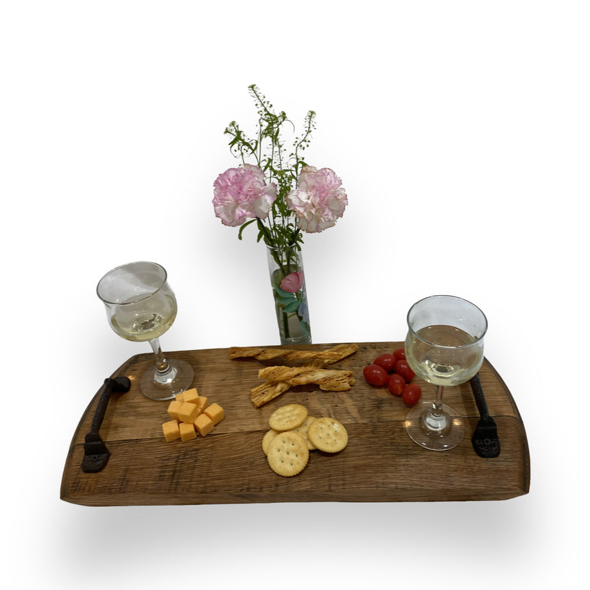 The Charcuterie and Cheese Rectangle Wooden Serving Board, full size and hand made from solid wood, holds wine, cheese, crackers, breadsticks, and cherry tomatoes next to a pink floral vase for rustic charm.