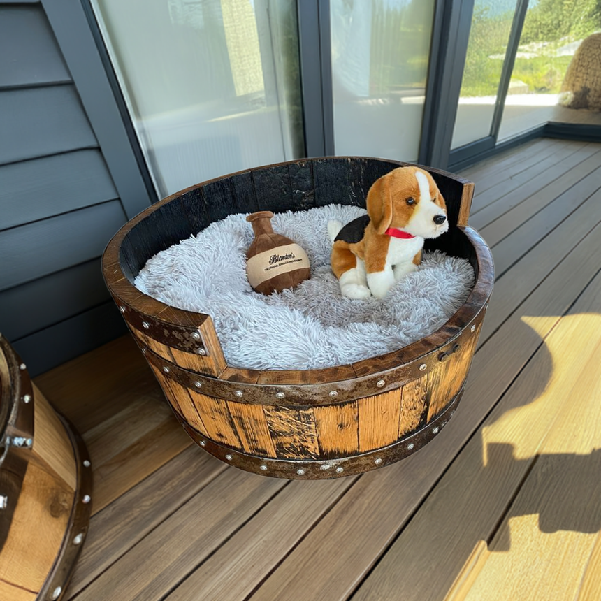 A plush beagle toy and a stuffed football rest in a Dog Bed Wooden, Round Frame with hand-made solid wood barrel construction, on a deck.