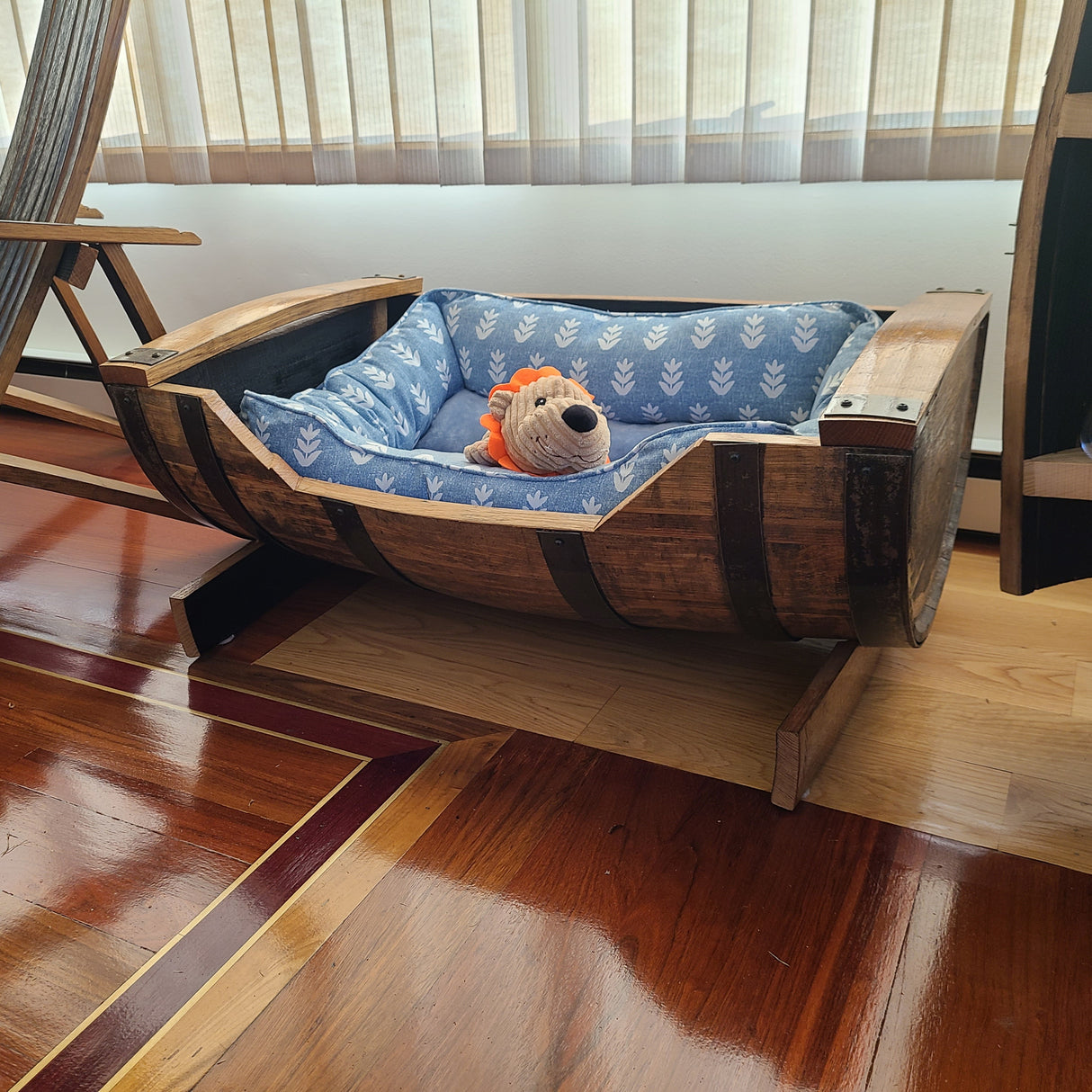 Immerse your pet in luxury with the Dog Bed - A005, a stylish wooden barrel featuring a cozy blue cushion and a charming stuffed lion toy inside, perfectly suited for a room with wooden floors. Priced at $225.