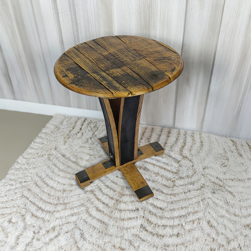 The End Table, handcrafted from whiskey barrels with a rustic finish, stands on a patterned rug against a light wood wall—adding timeless rustic charm to any space.