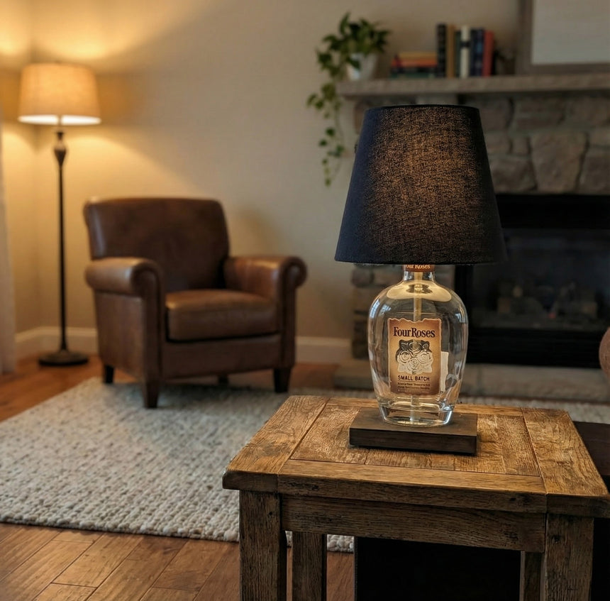A Four Roses Lamp crafted from repurposed bottles adds rustic elegance to a cozy living room, sitting on a wooden side table beside an armchair and fireplace.