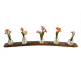 Five glass vases with pink flowers are displayed on a curved Bud Vase Stand made from reclaimed whiskey barrels, set against a white background.