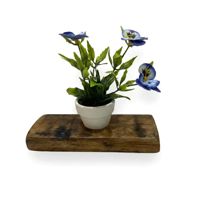 Single Bud Vase Whiskey Barrel Stave featuring a small white pot with blue artificial flowers and green leaves, set on a rustic reclaimed barrel stave shelf against a white background.