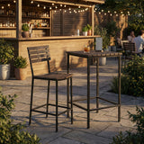 Outdoor bar scene at sunset featuring the Outdoor Bar Stool at a high table, with a cocktail and string lights glowing in the background.