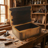 A Small Stave Box rests open on a workbench in a rustic woodworking shop, with tools and wood shavings scattered around.