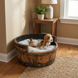 A plush toy dog rests in a Dog Bed Wooden, Round Frame, hand made with solid wood barrel construction, surrounded by a fluffy blanket and a toy bottle.