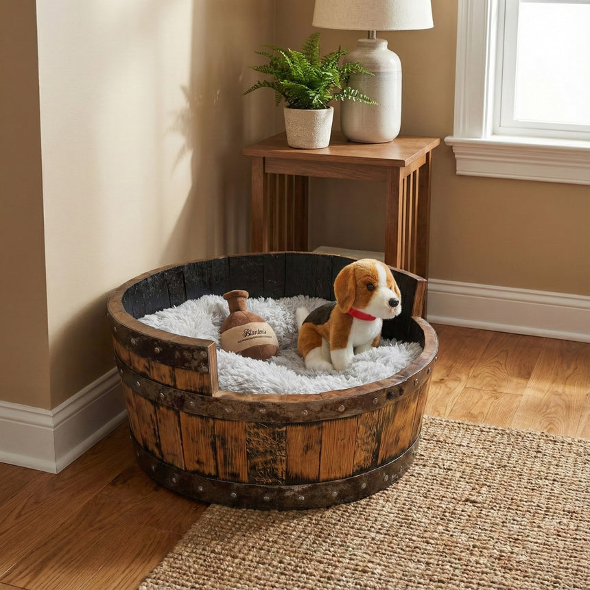 A plush toy dog rests in a Dog Bed Wooden, Round Frame, hand made with solid wood barrel construction, surrounded by a fluffy blanket and a toy bottle.