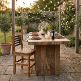 Rustic outdoor table set for dinner with candles, flowers, wine, and string lights in a garden setting, featuring elegant Barrel Dinner Chairs for a charming touch.