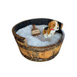 A plush dog sits in a cozy, round Dog Bed Wooden with hand made solid wood barrel construction, a soft cushion, and a small toy bottle.