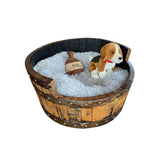 A plush dog sits in a cozy, round Dog Bed Wooden with hand made solid wood barrel construction, a soft cushion, and a small toy bottle.