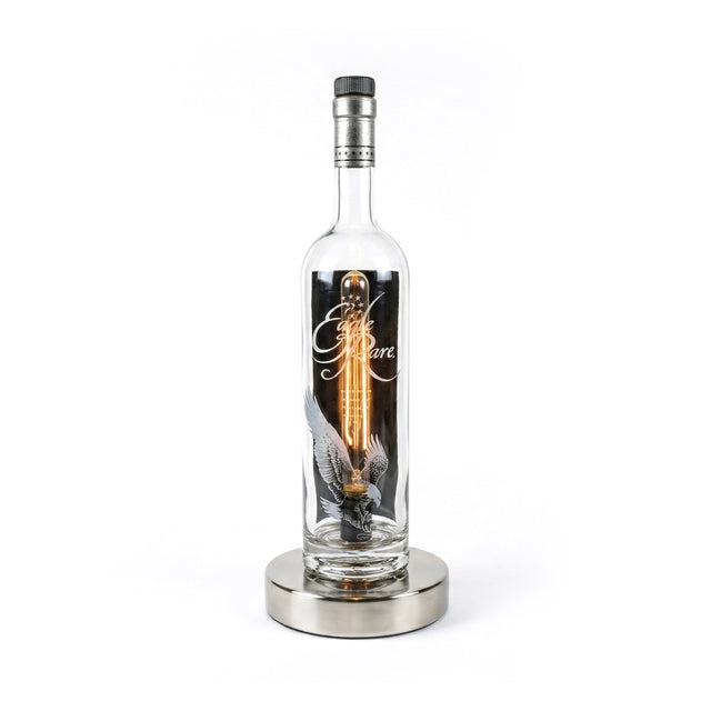 The Eagle Rare Lamp features a clear glass bourbon bottle with an exposed bulb, resting on a round metallic base, adding vintage charm to any space.