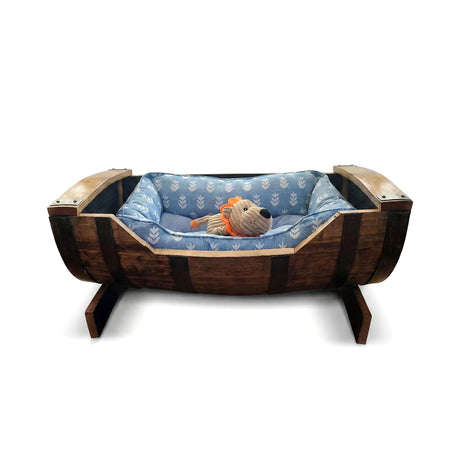 A plush toy lion rests in a blue cushioned Dog Bed Wooden, handmade from a solid wood barrel frame—perfect for small and medium-sized dogs.