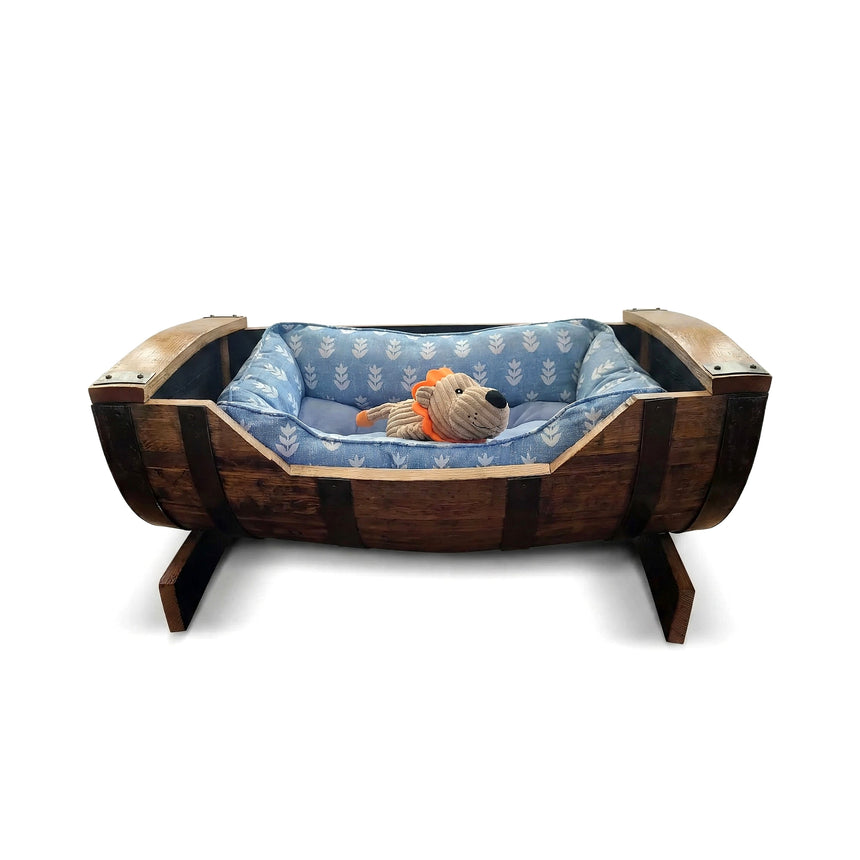 A plush toy lion rests in a blue cushioned Dog Bed Wooden, handmade from a solid wood barrel frame—perfect for small and medium-sized dogs.