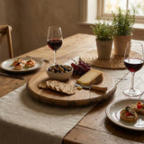 A Lazy Susan Round Swivel Wooden Tray, hand made from solid wood barrel head, holds wine, cheese, crackers, olives, grapes, and bruschetta on a rustic table set near a sunny window.