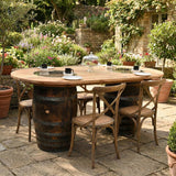 The Double Barrel Table set with four chairs is arranged in a lush garden patio, surrounded by blooming flowers.
