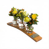 Three small glass vases with yellow flowers and greenery sit on the Bud Vase Stand, crafted from reclaimed whiskey barrels and accented with metal details.