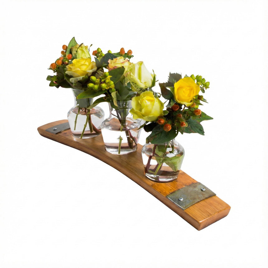 Three small glass vases with yellow flowers and greenery sit on the Bud Vase Stand, crafted from reclaimed whiskey barrels and accented with metal details.