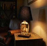 The Four Roses Lamp, crafted from repurposed Four Roses bottles, brings rustic elegance to a wooden table next to a leather chair.