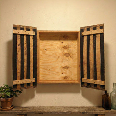 The handcrafted Dart Board Cabinet, made from solid wood barrel staves and fitting a standard tournament spec dart board, sits above a shelf with decor—an ideal game room accent.